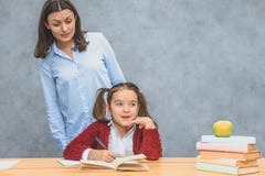 Mama i c?rka na szarym tle W tym samym czasie pisze pracie domowej uczeń, matka ogląda ona c?rka zdjęcia stock Mama i c?rka na szarym tle W tym samym czasie pisze pracie domowej uczeń, matka ogląda ona c?rka zdjęcia stock