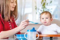 Mamma die de hand van de babyholding met een lepel van havermoutpap voeden Emoties van een kind terwijl het eten van gezond voeds stock fotografie Mamma die de hand van de babyholding met een lepel van havermoutpap voeden Emoties van een kind terwijl het eten van gezond voeds stock fotografie