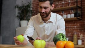 Man browsing on mobile phone at home kitchen. Handsome young man browsing on smartphone smiling happy. A man eats an stock video Man browsing on mobile phone at home kitchen. Handsome young man browsing on smartphone smiling happy. A man eats an stock video