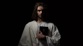 Man in crown of thorns holding bible looking directly, Jesus before crucifixion