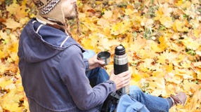 Man with cup of hot drink - tea or coffee and thermos sits in autumn forest with backpack, rear view stock photography Man with cup of hot drink - tea or coffee and thermos sits in autumn forest with backpack, rear view stock photography