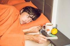Man feeling cold, lying in the bed and drinks tea and measures t stock photos Man feeling cold, lying in the bed and drinks tea and measures t stock photos