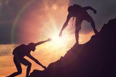 Man is giving helping hand. Silhouettes of people climbing on mountain at sunset