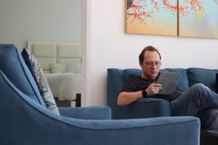 A man with glasses is working on a tablet. man relaxing in room sitting on the couch. Interested attractive man sitting on a sofa royalty free stock image A man with glasses is working on a tablet. man relaxing in room sitting on the couch. Interested attractive man sitting on a sofa royalty free stock image