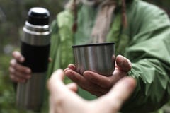 Man in green jacket offers a hot drink - tea or coffee from thermos to someone who pulls a hand, first person view royalty free stock photography Man in green jacket offers a hot drink - tea or coffee from thermos to someone who pulls a hand, first person view royalty free stock photography