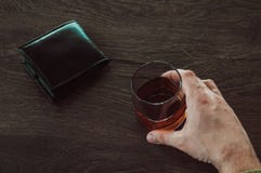 A man holding a glass of whiskey. Male hands holding a glass cup with cognac. A glass with alcohol and a wallet are on the table royalty free stock image A man holding a glass of whiskey. Male hands holding a glass cup with cognac. A glass with alcohol and a wallet are on the table royalty free stock image
