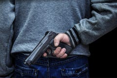 Man holding a gun behind his back against a black background. concept of danger, crime