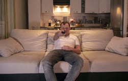 Man at home sitting on a sofa in the evening with the remote control in his hand, looking directly at the camera royalty free stock photos Man at home sitting on a sofa in the evening with the remote control in his hand, looking directly at the camera royalty free stock photos