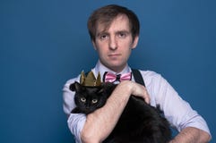 Man i den rosa skjortan, suspenderen och flugan som rymmer den gulliga svarta katten i skinande guld- krona royaltyfri foto Man i den rosa skjortan, suspenderen och flugan som rymmer den gulliga svarta katten i skinande guld- krona royaltyfri foto
