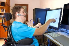 Man with infantile cerebral palsy using a computer. Spastic young man with infantile cerebral palsy caused by a complicated birth sitting in a multifunctional Man with infantile cerebral palsy using a computer. Spastic young man with infantile cerebral palsy caused by a complicated birth sitting in a multifunctional