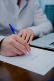 A man writes with a pen on a sheet of paper, visible computer. royalty free stock images A man writes with a pen on a sheet of paper, visible computer. royalty free stock images