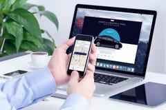 Man Orders Uber By IPhone And Macbook With Website On Background Man Orders Uber By IPhone And Macbook With Website On Background