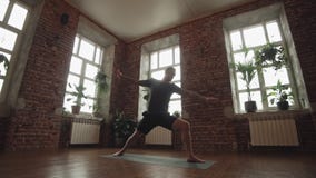 Man practice warrior yoga pose in studio with brick wall and large windows