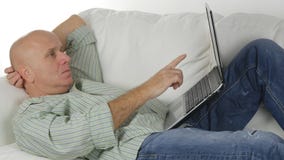 Man på en soffa som ser oroad till en bärbar dator som pekar med fingret royaltyfri bild Man på en soffa som ser oroad till en bärbar dator som pekar med fingret royaltyfri bild