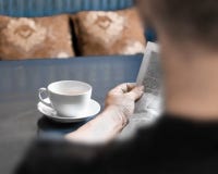 A man reading newspaper and drinking coffee sitting in cafe or at home in kitchen at morning time. A coffee cup on dark blue table royalty free stock photo A man reading newspaper and drinking coffee sitting in cafe or at home in kitchen at morning time. A coffee cup on dark blue table royalty free stock photo