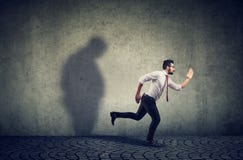 Man running away from his sad gloomy fat shadow on the wall royalty free stock photos Man running away from his sad gloomy fat shadow on the wall royalty free stock photos