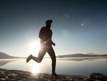 Man running on beach against backdrop of a beautiful sunset. Sand of mountain lake Stock Photo Man running on beach against backdrop of a beautiful sunset. Sand of mountain lake Stock Photo