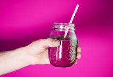 Man`s hand holding a glass jar with berry smoothie on the white wall background. royalty free stock images Man`s hand holding a glass jar with berry smoothie on the white wall background. royalty free stock images