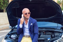 Man sited on his car with open hood happy talking by phone stock image Man sited on his car with open hood happy talking by phone stock image