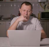 Man is sitting in the evening in the kitchen with a laptop stock photo Man is sitting in the evening in the kitchen with a laptop stock photo
