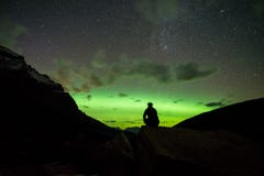Man sitting on a rock in the mountains watching the Northern Lights