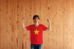 Man som b?r Vietnam flaggaf?rg av skjortan och st?r med den lyftta b?de n?ven p? tr?v?ggbakgrunden royaltyfri bild Man som b?r Vietnam flaggaf?rg av skjortan och st?r med den lyftta b?de n?ven p? tr?v?ggbakgrunden royaltyfri bild