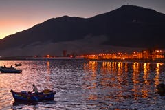 Man standing in boat rowing at late evening with coastal lights and mountains in background. Chimbote, Peru - April 17, 2018: Man standing in boat rowing at late Royalty Free Stock Photo Man standing in boat rowing at late evening with coastal lights and mountains in background. Chimbote, Peru - April 17, 2018: Man standing in boat rowing at late Royalty Free Stock Photo