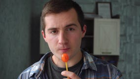 A man sucking an orange lollipop