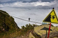 Man walking on suspension bridge and looking at cloudy mountains below. royalty free stock photo Man walking on suspension bridge and looking at cloudy mountains below. royalty free stock photo
