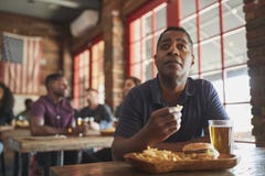 Man Watching Game On Screen In Sports Bar Eating Burger And Fries royalty free stock photo Man Watching Game On Screen In Sports Bar Eating Burger And Fries royalty free stock photo