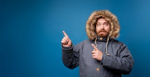 Man in winter jacket with fur on empty blue background in studio