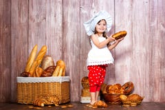 Mangez du pain frais et des pâtisseries faites maison Peu fille de sourire dans un chapeau de cuisinier avec le bagel à dispositi image stock Mangez du pain frais et des pâtisseries faites maison Peu fille de sourire dans un chapeau de cuisinier avec le bagel à dispositi image stock