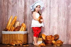 Mangez du pain frais et des pâtisseries faites maison Peu fille de sourire dans un chapeau de cuisinier avec le bagel à dispositi photo stock Mangez du pain frais et des pâtisseries faites maison Peu fille de sourire dans un chapeau de cuisinier avec le bagel à dispositi photo stock