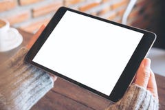 Mani che tengono il pc nero della compressa con lo schermo bianco in bianco con la tazza di caffè macchiato sulla tavola di legno Fotografia Stock Libera da Diritti Mani che tengono il pc nero della compressa con lo schermo bianco in bianco con la tazza di caffè macchiato sulla tavola di legno Fotografia Stock Libera da Diritti
