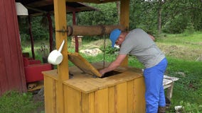 Maniglia agricola maschio della puleggia della casa del pozzo di rotazione da aumentare secchio sulla catena 4K stock footage Maniglia agricola maschio della puleggia della casa del pozzo di rotazione da aumentare secchio sulla catena 4K stock footage
