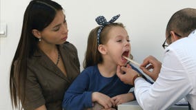 Manlig pediatrisk undersökande hals av liten flickasammanträde med hennes mamma royaltyfria bilder Manlig pediatrisk undersökande hals av liten flickasammanträde med hennes mamma royaltyfria bilder