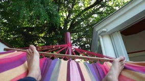 Mann, der auf einer bunten Hängematte an einem Sommertag sich entspannt Junger Kerl, der ein liegt Haar, herunternehmend Kreuzung stock footage Mann, der auf einer bunten Hängematte an einem Sommertag sich entspannt Junger Kerl, der ein liegt Haar, herunternehmend Kreuzung stock footage