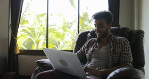 Mann, der im Lehnsessel unter Verwendung Laptop-Computer Schreibenzu hause arbeiten, Guy Surfing Internet Happy Smiling sitzt stock video footage Mann, der im Lehnsessel unter Verwendung Laptop-Computer Schreibenzu hause arbeiten, Guy Surfing Internet Happy Smiling sitzt stock video footage