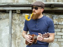 Mann mit dem Bart, der Ukulele spielt und ein Rohr raucht Stockbild Mann mit dem Bart, der Ukulele spielt und ein Rohr raucht Stockbild