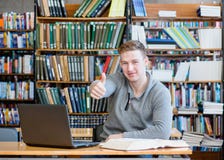 Mannelijke student met laptop die duimen in de universitaire bibliotheek tonen Royalty-vrije Stock Afbeelding Mannelijke student met laptop die duimen in de universitaire bibliotheek tonen Royalty-vrije Stock Afbeelding