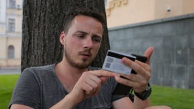Mannen med kreditkorten under shopping till och med internet som använder den smarta telefonen parkerar in, sammanträde under ett Mannen med kreditkorten under shopping till och med internet som använder den smarta telefonen parkerar in, sammanträde under ett