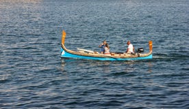 Mannen och kvinnan simmar i traditionellt maltese fartyg med den stränga kaptenen och tafotoet arkivfoton Mannen och kvinnan simmar i traditionellt maltese fartyg med den stränga kaptenen och tafotoet arkivfoton