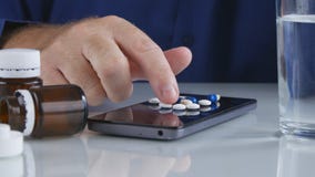 Mannen väljer och tar medicinska piller för huvudvärk från mobiltelefonskärmyttersida arkivfoto Mannen väljer och tar medicinska piller för huvudvärk från mobiltelefonskärmyttersida arkivfoto