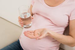 Mano de la mujer embarazada con el vidrio de la píldora del agua y de la vitamina imágenes de archivo libres de regalías Mano de la mujer embarazada con el vidrio de la píldora del agua y de la vitamina imágenes de archivo libres de regalías