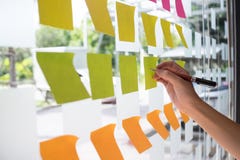 Mano facendo uso della nota appiccicosa di Post-it con 'brainstorming' sulla carta per appunti fotografie stock Mano facendo uso della nota appiccicosa di Post-it con 'brainstorming' sulla carta per appunti fotografie stock