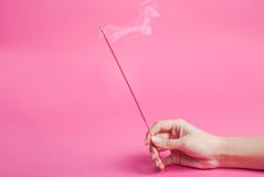 Mano femenina que sostiene los palillos del incienso que fuma en fondo rosado imagenes de archivo Mano femenina que sostiene los palillos del incienso que fuma en fondo rosado imagenes de archivo