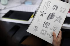 Mano que sostiene el cuaderno con las ideas de Drew Brand Logo Creative Design foto de archivo libre de regalías Mano que sostiene el cuaderno con las ideas de Drew Brand Logo Creative Design foto de archivo libre de regalías