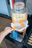 Manos de la mujer que tiran abajo de la palanca del dispensador del agua con agua infundida fruta foto de archivo Manos de la mujer que tiran abajo de la palanca del dispensador del agua con agua infundida fruta foto de archivo