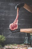 Manos masculinas del filete de carne de vaca de la hacha de guerra de la tenencia del carnicero o del cocinero en fondo rústico o fotos de archivo libres de regalías Manos masculinas del filete de carne de vaca de la hacha de guerra de la tenencia del carnicero o del cocinero en fondo rústico o fotos de archivo libres de regalías