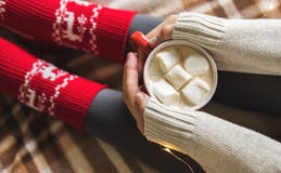 Manos y pies del ` s de las mujeres en el suéter y los calcetines rojos acogedores de lana que sostienen la taza de café caliente foto de archivo Manos y pies del ` s de las mujeres en el suéter y los calcetines rojos acogedores de lana que sostienen la taza de café caliente foto de archivo